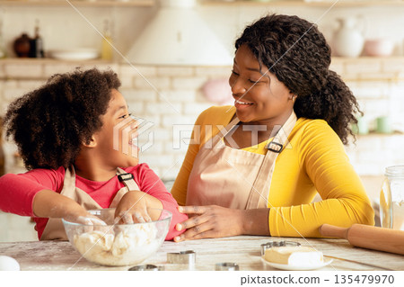 Black mom and little daughter baking in kitchen, african american family preparing dough for cookies and having fun at home, mother and her pretty female child chatting and laughing together, closeup 135479970