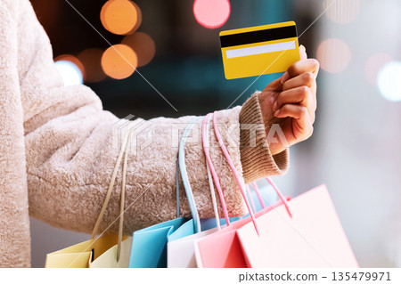Easy Payment Concept. Closeup Of Unrecognizable Black Woman In Winter Coat Holding Credit Card And Bright Colorful Shopping Bags From Mall, Standing Outdoors In The Evening. Retail And Purchase 135479971