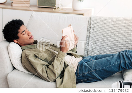 Distance education concept. Focused black teen student with textbook reading on sofa at home. African American teenager doing home assignment, getting ready for online test or exam Distance education concept. Focused black teen student with textbook reading on sofa at home. African American teenager doing home assignment, getting ready for online test or exam 135479982