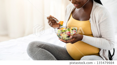 Happy Black Pregnant Woman Holding Bowl With Fresh Vegetable Salad, Enjoying Healthy Nutrition, Having Organic Vegetarian Meal For Lunch, Sitting On Bed At Home, Closeup Shot With Free Space 135479984