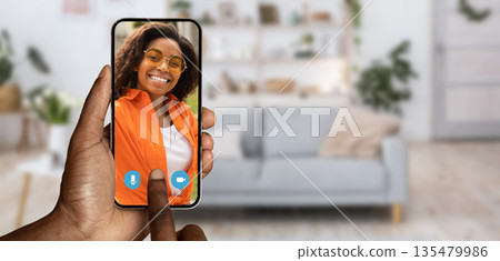 A person interacts with a smartphone, engaging in a video call from their home. The background features a comfortable living area, enhancing the cozy atmosphere of the conversation. A person interacts with a smartphone, engaging in a video call from their home. The background features a comfortable living area, enhancing the cozy atmosphere of the conversation. 135479986