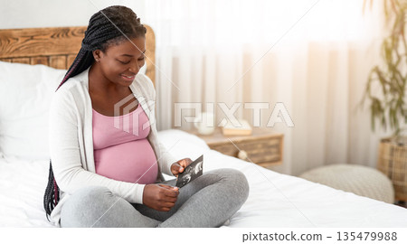 Happy African American Pregnant Lady Sitting On Bed With Baby Ultrasound Scan Image, Looking At Fetal Sonography Photo, Black Woman Enjoying Her Healthy Pregnancy And Future Maternity, Copy Space Happy African American Pregnant Lady Sitting On Bed With Baby Ultrasound Scan Image, Looking At Fetal Sonography Photo, Black Woman Enjoying Her Healthy Pregnancy And Future Maternity, Copy Space 135479988