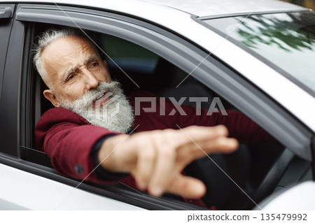 Nervous senior man driver fighting on the road, stuck in traffic, side view. Stressed aged grey-haired businessman yelling and gesturing while driving car, going for business meeting, free space 135479992