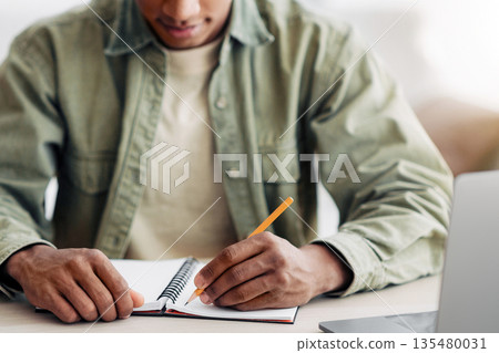 Remote learning concept. Black student writing in notebook during online lesson at home, focus on hands. Cropped view of African American youth participating in webinar, taking educational course Remote learning concept. Black student writing in notebook during online lesson at home, focus on hands. Cropped view of African American youth participating in webinar, taking educational course 135480031