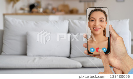 A person is using a smartphone to connect in a video call, showcasing a casual home environment. The individual on the screen appears happy and focused on the conversation. 135480096