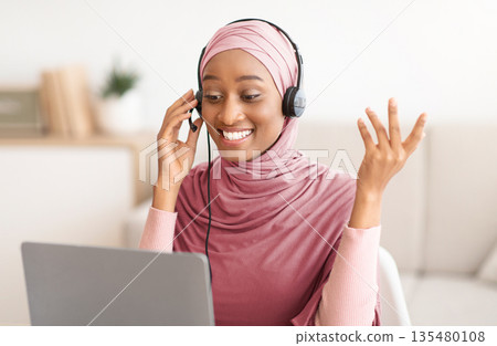 Online education. Young black female teacher in hijab having video lesson with students, using laptop webcam indoors. Happy Muslim tutor in headscarf giving webinar from home Online education. Young black female teacher in hijab having video lesson with students, using laptop webcam indoors. Happy Muslim tutor in headscarf giving webinar from home 135480108