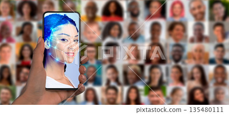 A person's hand holds a smartphone displaying facial recognition software. In the background, a collage of diverse faces represents modern identification technology and its impact on society today. 135480111