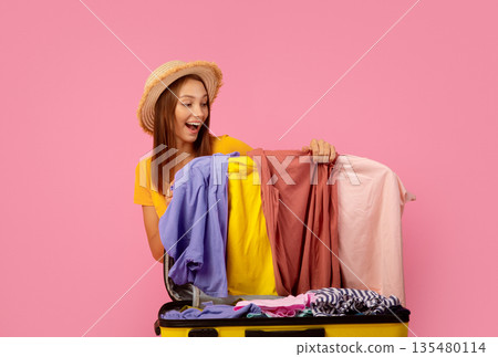 Excited young woman collecting clothes in suitcase before journey, pink background, copy space Excited young woman collecting clothes in suitcase before journey, pink background, copy space 135480114