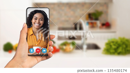 A person is enjoying a video call on a smartphone while sitting in a cozy kitchen. Recipient smiling and engaged. Telecommunication concept A person is enjoying a video call on a smartphone while sitting in a cozy kitchen. Recipient smiling and engaged. Telecommunication concept 135480174