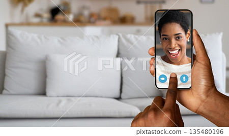 A person engages in an online video call with friend, using a smartphone, smiling as they talk. Comfortable home surroundings enhance the connection in this virtual communication. A person engages in an online video call with friend, using a smartphone, smiling as they talk. Comfortable home surroundings enhance the connection in this virtual communication. 135480196