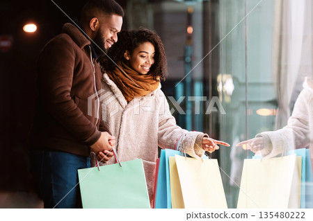 Let's Buy This. Cute lovely african american family of two choosing something in store standing outside, woman pointing at window, walking with her boyfriend or husband in the evening near mall Let's Buy This. Cute lovely african american family of two choosing something in store standing outside, woman pointing at window, walking with her boyfriend or husband in the evening near mall 135480222