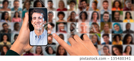 A person's hand holds a smartphone displaying a facial recognition scan of a smiling face. The background is a collage of diverse faces, showcasing modern technology in identification. A person's hand holds a smartphone displaying a facial recognition scan of a smiling face. The background is a collage of diverse faces, showcasing modern technology in identification. 135480341