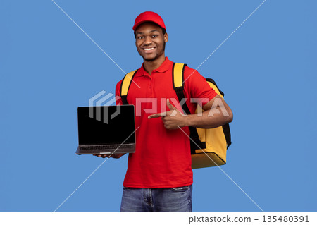 Order Here. Portrait of smiling black delivery man holding laptop and pointing at empty screen for mockup, wearing red uniform and yellow thermo backpack, standing on blue studio background, copyspace Order Here. Portrait of smiling black delivery man holding laptop and pointing at empty screen for mockup, wearing red uniform and yellow thermo backpack, standing on blue studio background, copyspace 135480391
