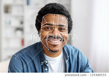 African American man is using facial recognition technology for identification at home. The digital overlay emphasizes facial features, showcasing advanced tech for seamless verification. African American man is using facial recognition technology for identification at home. The digital overlay emphasizes facial features, showcasing advanced tech for seamless verification. 135480555