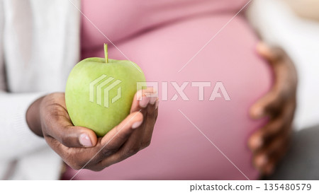 Black Pregnant Woman Holding Organic Green Apple, Enjoying Healthy Nutrition During Pregnancy, Unrecognizable Expectant Lady Having Vitamin Snack At Home, Cropped Image With Selective Focus, Closeup Black Pregnant Woman Holding Organic Green Apple, Enjoying Healthy Nutrition During Pregnancy, Unrecognizable Expectant Lady Having Vitamin Snack At Home, Cropped Image With Selective Focus, Closeup 135480579