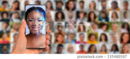 A person holds a smartphone displaying a face scan while surrounded by a collage of diverse portraits. This showcases the advancement of identification technology in daily life. A person holds a smartphone displaying a face scan while surrounded by a collage of diverse portraits. This showcases the advancement of identification technology in daily life. 135480587