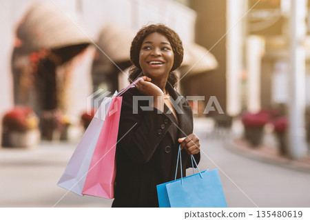 Great offer at low price during Black Friday and seasonal sales. Impressions smiling african american attractive woman in coat holding many packages and looking at something amazing or sale ad 135480619