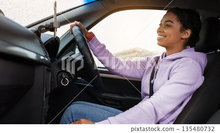 Great friendly taxi driver, auto blogger and car traveler. Smiling millennial african american woman holding steering wheel, changing speed, looking at road, driving car in rain, profile, empty space Great friendly taxi driver, auto blogger and car traveler. Smiling millennial african american woman holding steering wheel, changing speed, looking at road, driving car in rain, profile, empty space 135480732