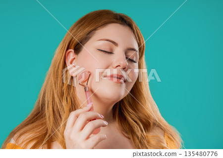 Plus Size Woman Doing Face Massage With Rose Quartz Stone Roller For Firmer Plus Size Woman Doing Face Massage With Rose Quartz Stone Roller For Firmer 135480776