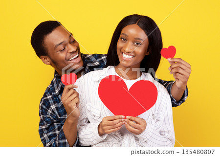 Valentines day, romantic and date. Happy young african american couple in love with hearts have fun together at spare time at covid-19 pandemic, isolated on yellow background, studio shot, copy space Valentines day, romantic and date. Happy young african american couple in love with hearts have fun together at spare time at covid-19 pandemic, isolated on yellow background, studio shot, copy space 135480807