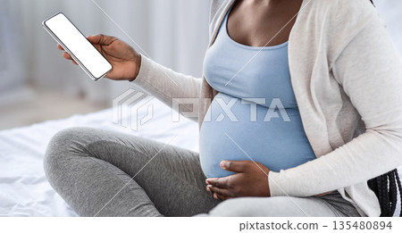 Unrecognizable African American Expectant Mother Using Smartphone With Black Screen At Home, Browsing Pregnancy App Or Shopping Online While Relaxing On Bed, Touching Her Pregnant Belly, Cropped Image Unrecognizable African American Expectant Mother Using Smartphone With Black Screen At Home, Browsing Pregnancy App Or Shopping Online While Relaxing On Bed, Touching Her Pregnant Belly, Cropped Image 135480894