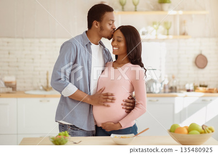 Maternity and healthy eating concept. Caring black husband kissing his pregnant wife in kitchen while cooking breakfast. Expectant African American couple having romantic moment at home Maternity and healthy eating concept. Caring black husband kissing his pregnant wife in kitchen while cooking breakfast. Expectant African American couple having romantic moment at home 135480925