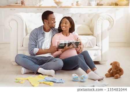 Young black couple expecting baby and writing checklist of child stuff for maternity hospital, sitting on floor in living room. Positive future parents making list for birthing center at home Young black couple expecting baby and writing checklist of child stuff for maternity hospital, sitting on floor in living room. Positive future parents making list for birthing center at home 135481044