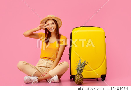 Happy woman in summer clothes with pineapple showing peace gesture, sitting by suitcase, posing on pink studio background. Carefree young lady travelling to exotic warm countries, hot deals Happy woman in summer clothes with pineapple showing peace gesture, sitting by suitcase, posing on pink studio background. Carefree young lady travelling to exotic warm countries, hot deals 135481084