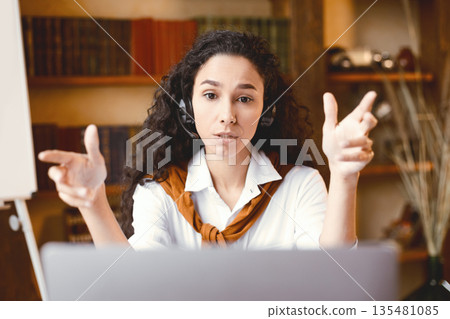Remote Work. Portrait of focused woman sitting at desk, having video call on laptop, explaining lesson to students or working and talking to colleagues and gesturing to webcam, consulting client 135481085