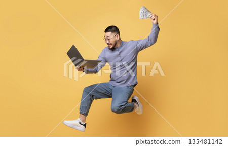 Big Profit. Excited Young Asian Man Jumping With Laptop And Dollar Cash In Hands On Yellow Background, Joyful Happy Millennial Guy Celebrating Successful Investment Or Online Lottery Win, Copy Space Big Profit. Excited Young Asian Man Jumping With Laptop And Dollar Cash In Hands On Yellow Background, Joyful Happy Millennial Guy Celebrating Successful Investment Or Online Lottery Win, Copy Space 135481142