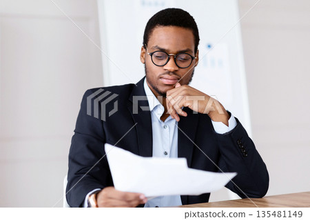 Pensive black manager, businessman sitting in his office in front of laptop, reading papers marketing report, having financial troubles, copy space. Problems with business, bankruptcy, crisis, concept Pensive black manager, businessman sitting in his office in front of laptop, reading papers marketing report, having financial troubles, copy space. Problems with business, bankruptcy, crisis, concept 135481149