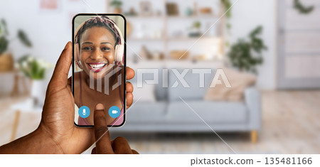 A person engaged in a video call using a smartphone shows a smiling face on the screen. Bright decor and a comfortable couch create a warm home atmosphere, enhancing connectivity. A person engaged in a video call using a smartphone shows a smiling face on the screen. Bright decor and a comfortable couch create a warm home atmosphere, enhancing connectivity. 135481166