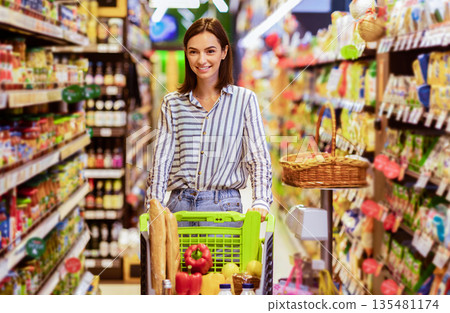 Everyday Shopping. Portrait Of Young Housewife Walking With Trolley Cart Between The Aisles In Wholesale Store. Casual Woman Buying Healthy Food In Shop, Looking At Shelves, Blurred Background Everyday Shopping. Portrait Of Young Housewife Walking With Trolley Cart Between The Aisles In Wholesale Store. Casual Woman Buying Healthy Food In Shop, Looking At Shelves, Blurred Background 135481174