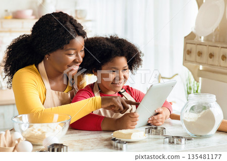 Happy Black Mom And Little Daughter Using Digital Table In Kitchen Together, Checking Recipe Of Dough Online While Preparing Pastry, African American Family Cooking At Home And Having Fun , Free Space 135481177
