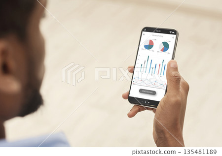 Cropped of black man using analytics mobile app on smartphone, checking his incomes on trading stocks, panorama. Male hands holding phone with newest analytics mobile application 135481189