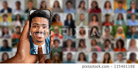 A hand holds a smartphone displaying a face recognition scan of a smiling man. Behind are various blurred portraits of people, illustrating advanced identification technology in action. A hand holds a smartphone displaying a face recognition scan of a smiling man. Behind are various blurred portraits of people, illustrating advanced identification technology in action. 135481198