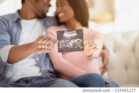 Positive black couple showing ultrasound photo of their unborn baby at home, selective focus on hands. Happy expectant family with sonogram of their child, creating happy memories together Positive black couple showing ultrasound photo of their unborn baby at home, selective focus on hands. Happy expectant family with sonogram of their child, creating happy memories together 135481217