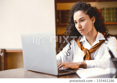 Distance Education. Portrait of confident lady sitting at desk, using laptop computer, typing on keyboard. Woman studying or teaching online at home, doing homework, chatting with tutor or students 135481286