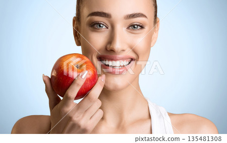 Stomatology Concept. Woman With Perfect Smile Holding Red Apple, Blue Background Stomatology Concept. Woman With Perfect Smile Holding Red Apple, Blue Background 135481308