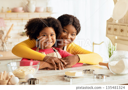 Portraif Of Loving Black Family Mom And Daughter In Aprons Posing At Table In Kitchen While Baking Together, African American Mother And Her Child Enjoying Cooking Homemade Food, Free Space Portraif Of Loving Black Family Mom And Daughter In Aprons Posing At Table In Kitchen While Baking Together, African American Mother And Her Child Enjoying Cooking Homemade Food, Free Space 135481324