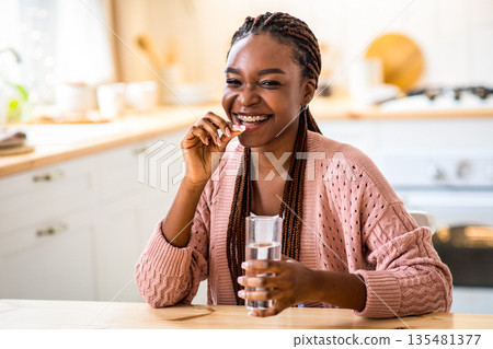 Cheerful Young African American Lady Taking Beauty Supplement Pill In Kitchen, Happy Black Millennial Woman Sitting At Tablet, Eating Multivitamin Tablet And Drinking Water At Home, Free Space Cheerful Young African American Lady Taking Beauty Supplement Pill In Kitchen, Happy Black Millennial Woman Sitting At Tablet, Eating Multivitamin Tablet And Drinking Water At Home, Free Space 135481377