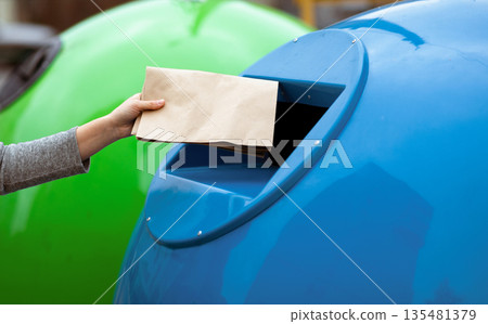 Waste Sorting. Unrecognizable Lady Throwing Paper Bag Into Blue Garbage Recycle Bin Outdoors, Woman Enjoying Separating Garbage, Caring About Environment, Cropped Image With Selective Focus Waste Sorting. Unrecognizable Lady Throwing Paper Bag Into Blue Garbage Recycle Bin Outdoors, Woman Enjoying Separating Garbage, Caring About Environment, Cropped Image With Selective Focus 135481379