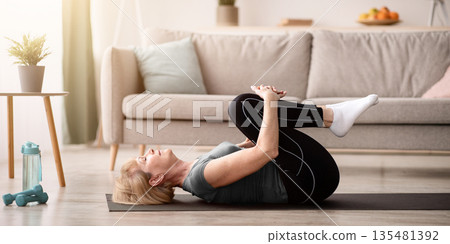 Sporty senior woman doing exercises on yoga mat indoors, blank space. Full length of fit mature lady working out at home during covid pandemic, relaxing her back muscles 135481392