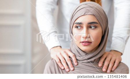 Arab Husband Threatening Scared Wife In Hijab Touching Her Shoulders Standing Behind Her Back At Home. Domestic Violence And Abuse, Unhappy Marriage With Abuser Problem. Cropped, Selective Focus Arab Husband Threatening Scared Wife In Hijab Touching Her Shoulders Standing Behind Her Back At Home. Domestic Violence And Abuse, Unhappy Marriage With Abuser Problem. Cropped, Selective Focus 135481406