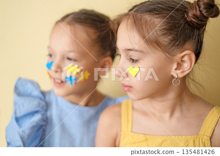 A girl with down syndrome with yellow-blue puzzles on face next to her thoughtful sister A girl with down syndrome with yellow-blue puzzles on face next to her thoughtful sister 135481426