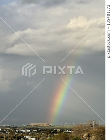 Rainbow over landscape. Rainbow over landscape under cloudy sky. Rainbow over landscape. Rainbow over landscape under cloudy sky. 135481572