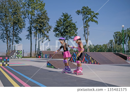 Children are roller skating in the city's outdoor skate park holding hands. Children are roller skating in the city's outdoor skate park holding hands. 135481575