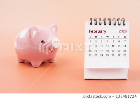 Desk calendar for February 2026 and pink piggy bank. 135481724