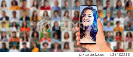 A person holds a smartphone that shows a facial recognition scan of their face. Behind them, a diverse crowd is visible, highlighting modern identification technology in action. 135482218