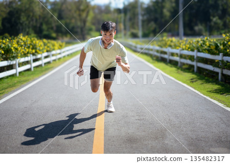 Man running at full speed on an open road, expressing energy, effort, and strong commitment after the moment of starting. 135482317